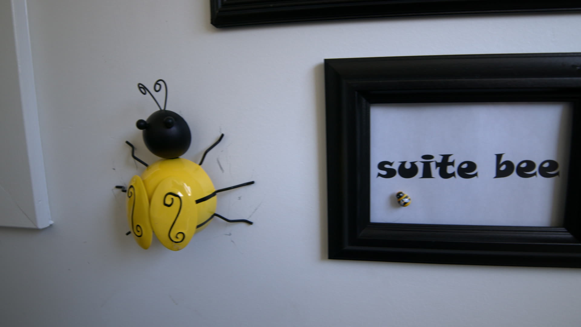Black framed 'suite bee' sign beside a yellow bee on the wall