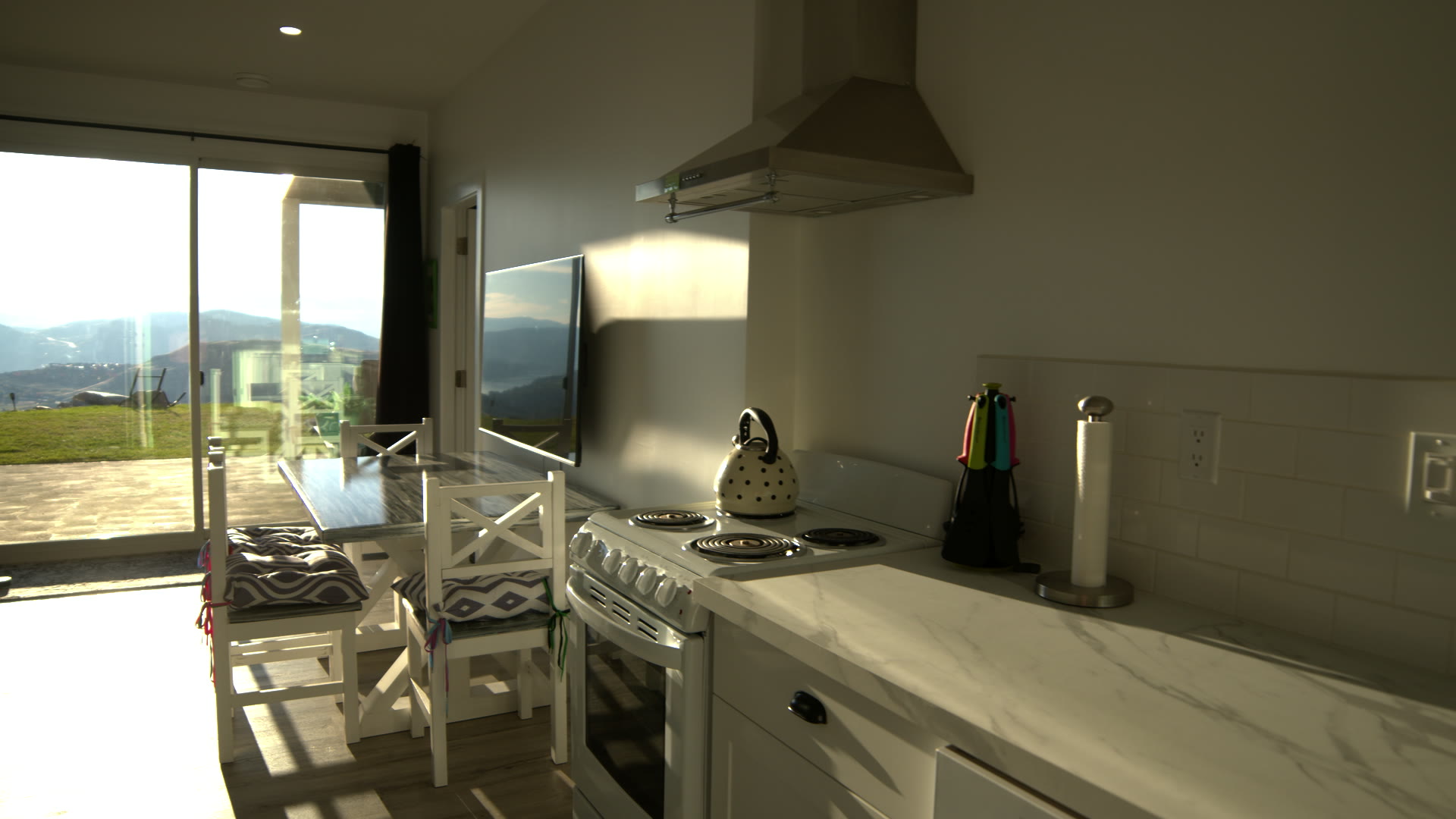 Kitchen: white counters and subway tile, the kettle on the stove, the patio door and the valley beyond
